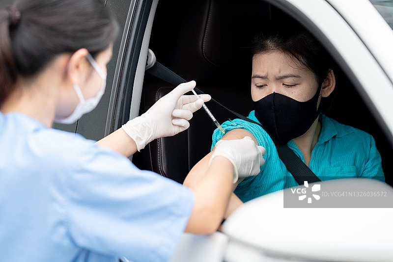 驾车接种疫苗点，亚洲年轻医生为驾车人士注射新冠疫苗图片素材