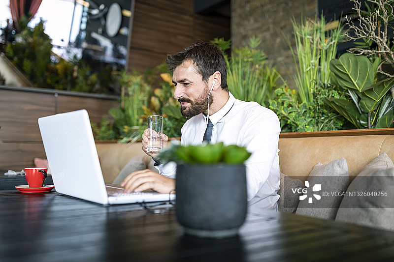 一位年轻的商务男士在现代咖啡厅使用笔记本电脑，与同事交流并饮用新鲜水图片素材