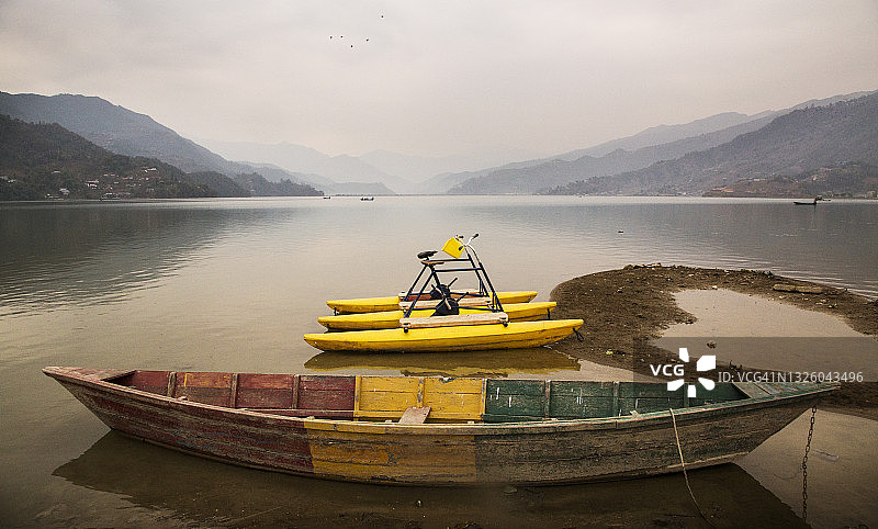 尼泊尔博卡拉费瓦湖畔宁静祥和的日出景象，五彩小船和独木舟倒映在湖面上图片素材