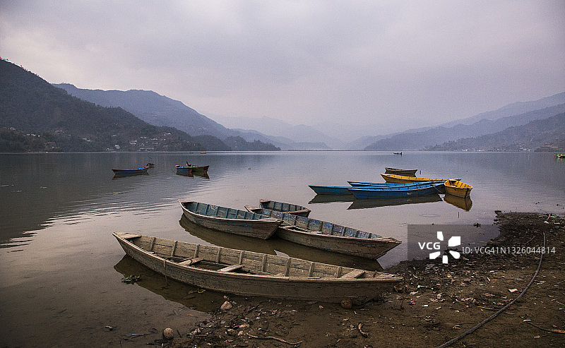 尼泊尔博克拉费瓦湖上五彩船只和独木舟在朦胧的清晨倒映在水面上，宁静祥和的日出景色图片素材