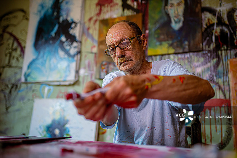 潮人老年艺术家在画布上挤压红色油画颜料管图片素材