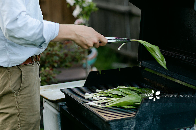 男人将调味过的野韭菜放在烤架上图片素材