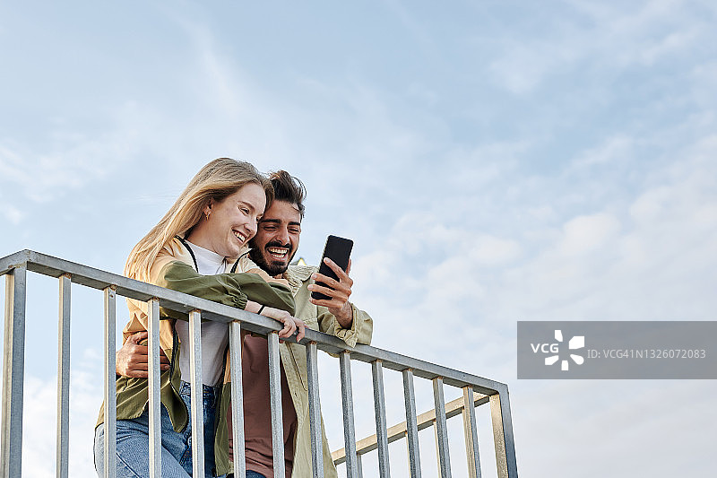 年轻的混血夫妇看着手机微笑图片素材