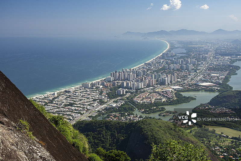 从雨林山丘俯瞰城市海岸建筑的绿色美景图片素材