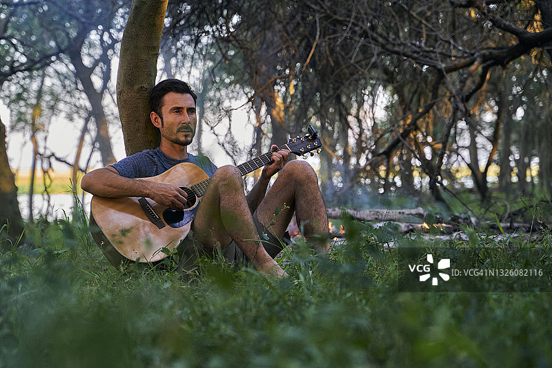 年轻男子坐在树上弹吉他图片素材