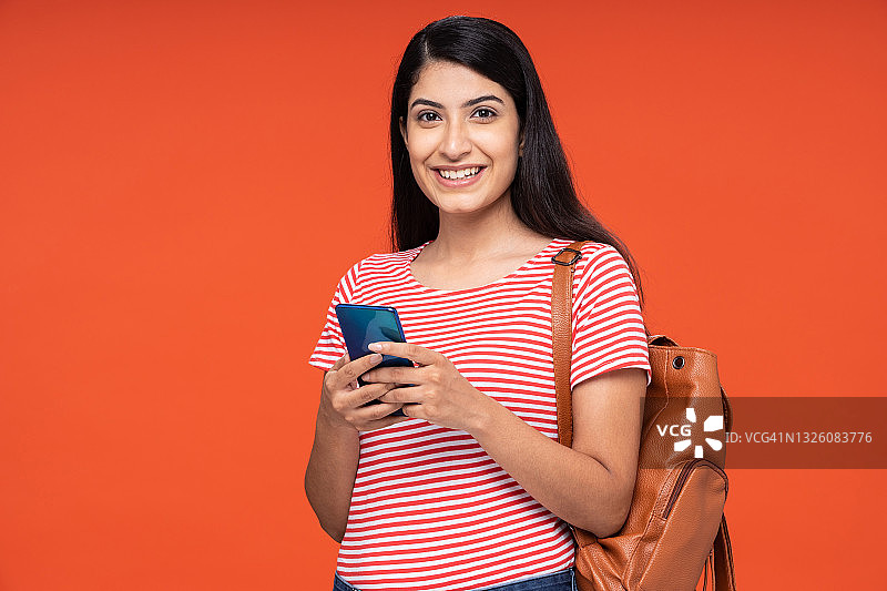 年轻女学生在红色背景中使用手机的肖像照片图片素材