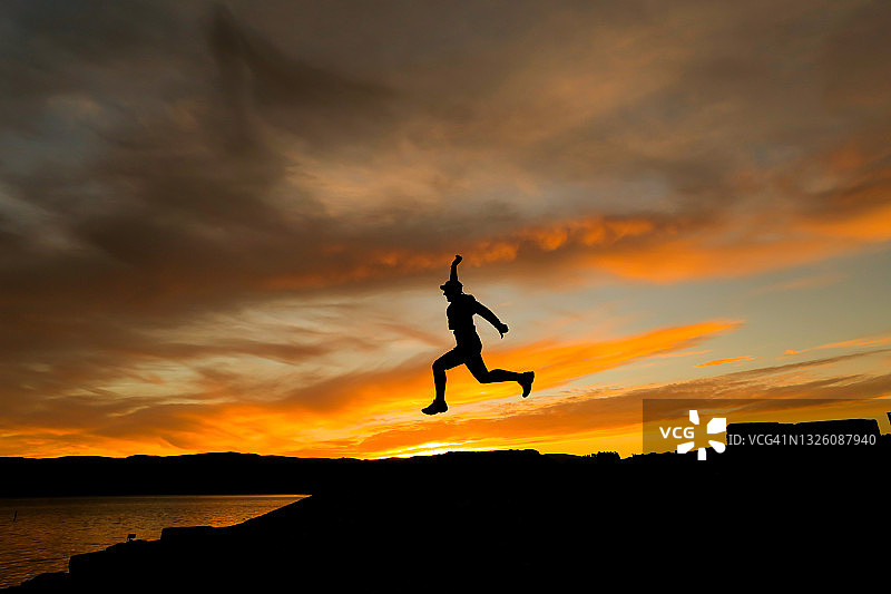 夕阳下戴帽男子跳跃的剪影图片素材