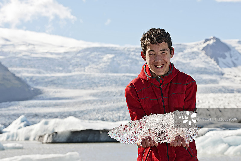 青少年男孩举起从冰岛冰川泻湖中取出的冰块图片素材