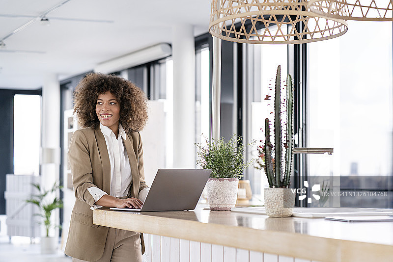在办公室自助餐厅柜台用笔记本电脑微笑的黑人女商人图片素材