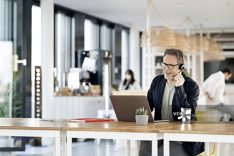 在自助餐厅通过耳机交谈的男性客服代表图片素材