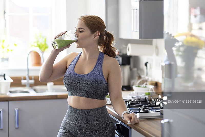 红发女人在家锻炼后喝健康奶昔图片素材