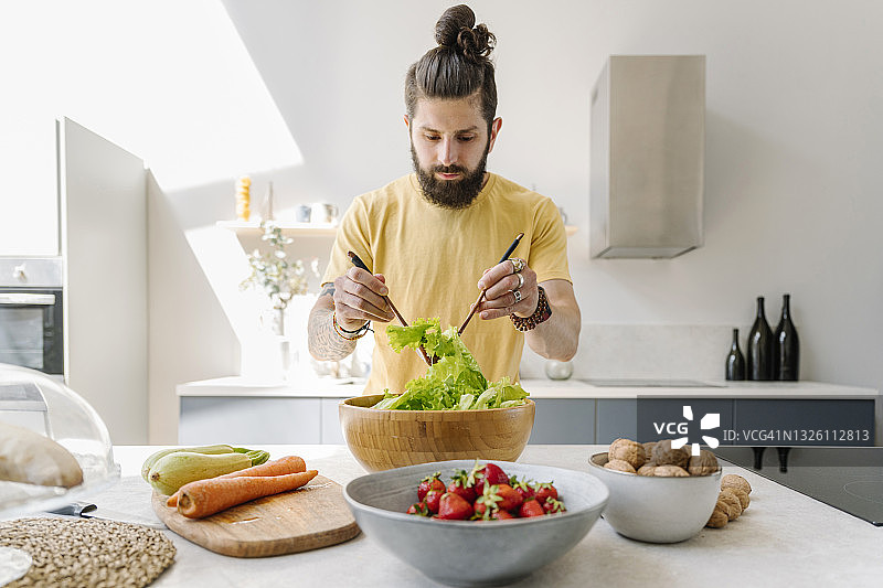 男人在家准备沙拉时搅拌蔬菜图片素材
