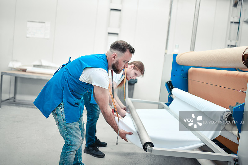 纺织厂里专注的纺织工人，在印刷机上折叠布料卷图片素材