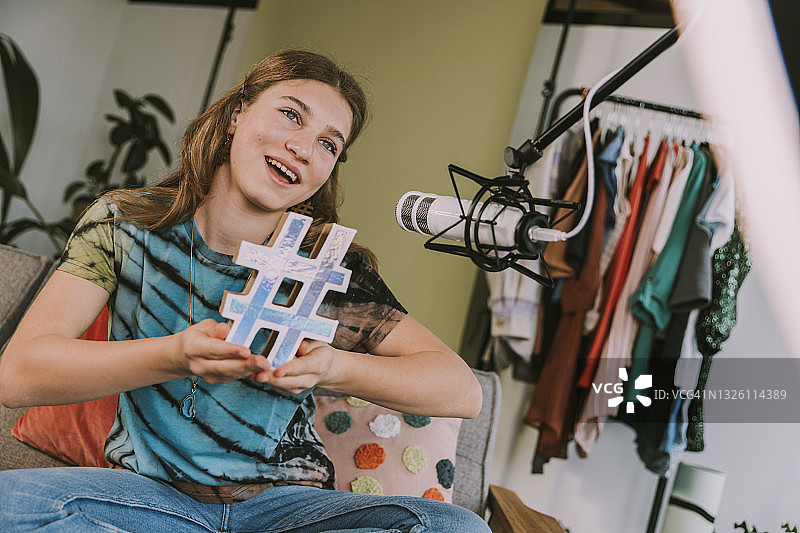 女性网红在家拍摄视频时举着话题标签符号图片素材