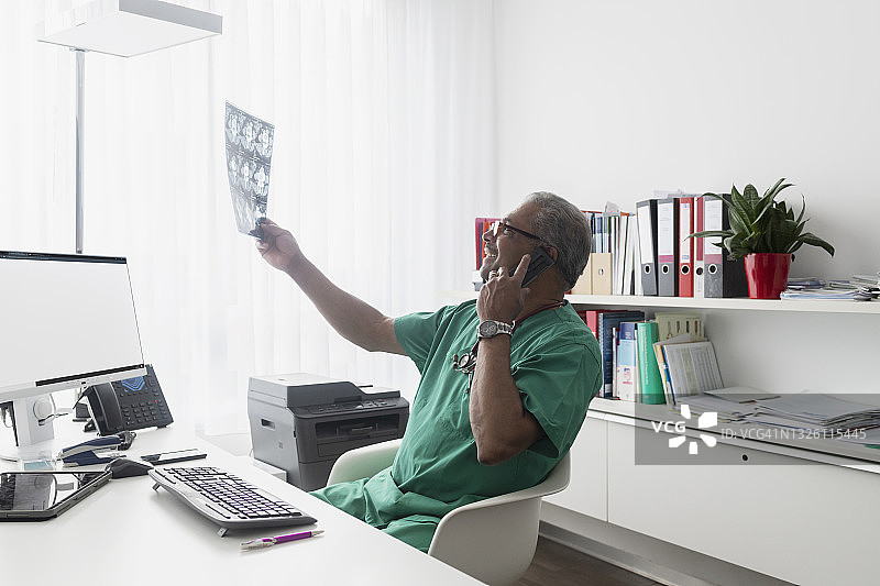 年长的外科医生查看CT X光片，与放射科医生通电话图片素材