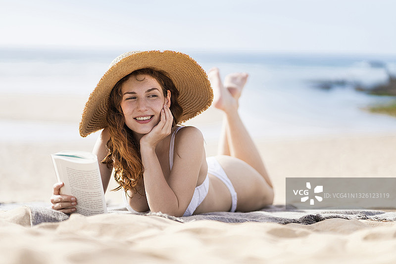 在阳光明媚的日子里躺在沙滩上做白日梦的微笑美丽女人图片素材