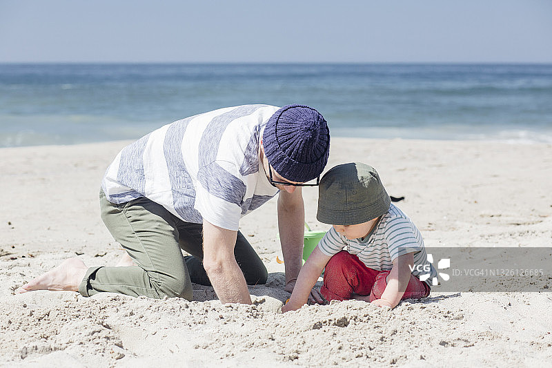 阳光明媚，父子在海滩上一起挖沙玩耍图片素材