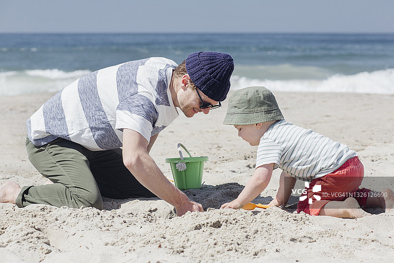 晴天，微笑的男人和儿子在海滩上挖沙子图片素材