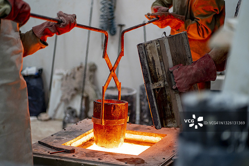 男性专家在青铜铸造厂用手动工具从炉中取出容器图片素材