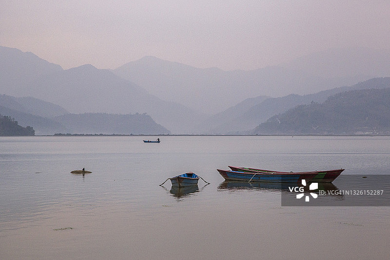 尼泊尔博克拉费瓦湖上，薄雾笼罩的清晨，停泊的独木舟倒映在湖面上，宁静祥和的日出美景图片素材