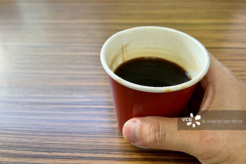 木桌上人手拿着的纸杯黑咖啡图片素材