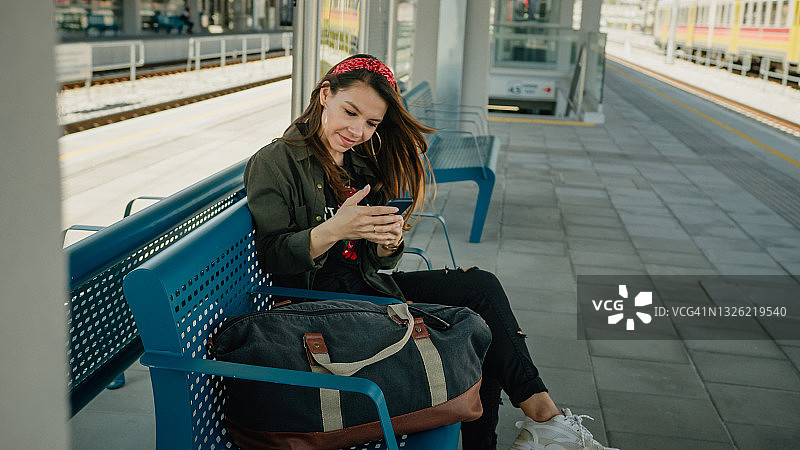 在站台上看智能手机的年轻漂亮女孩图片素材