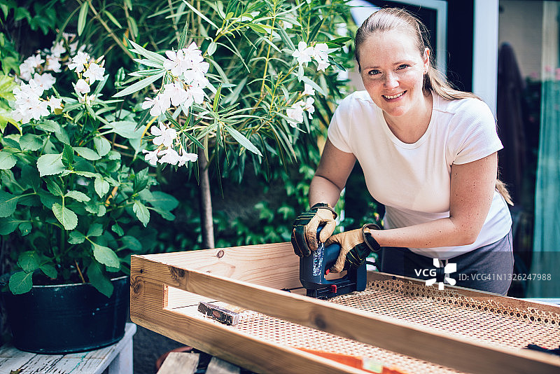 微笑的女人用订书机将藤条网固定在木制散热器罩上图片素材