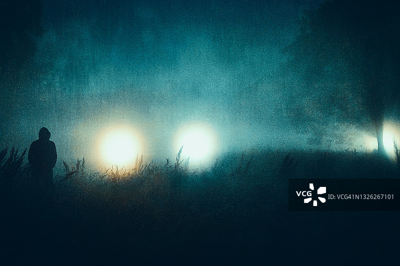 笼罩在神秘光芒下的戴兜帽人物恐怖概念图片素材