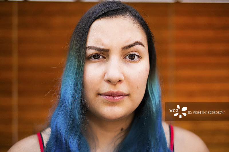 挑着眉毛看着镜头的年轻拉丁裔蓝发女子图片素材