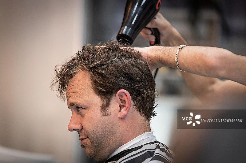 美发师在理发店为成年男人吹发图片素材