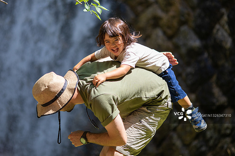 年轻女孩在瀑布边骑在父亲背上欢笑图片素材