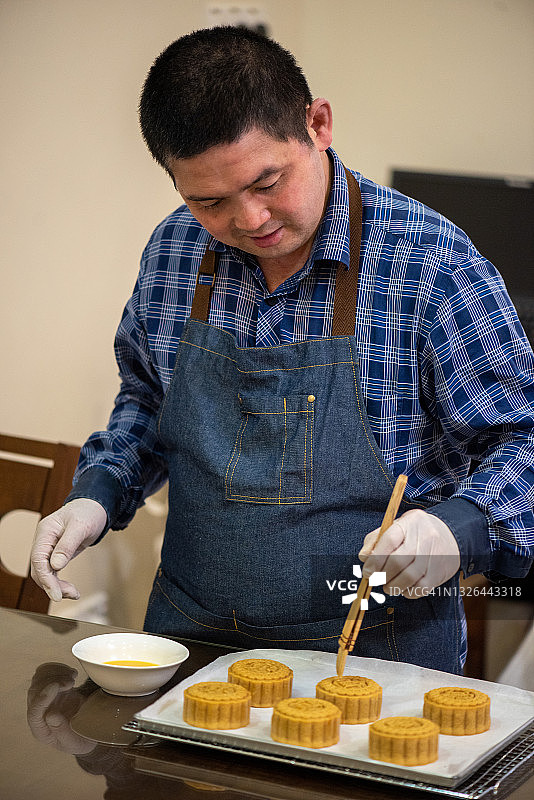 面包师在烤盘上用鸡蛋液涂抹面团，制作自制中式月饼图片素材