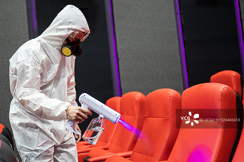 在电影放映前，亚洲华人卫生员戴着口罩在电影院大厅的椅子和地毯上进行消毒图片素材