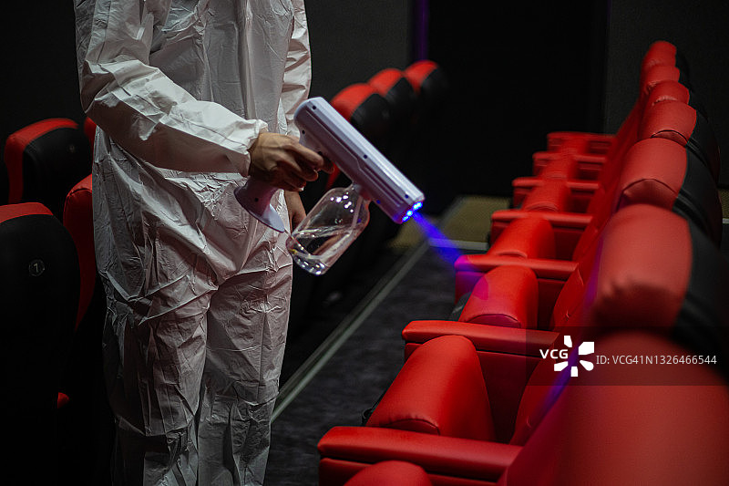 在电影放映前，亚洲华人卫生员戴着口罩在电影院大厅的椅子和地毯上进行消毒图片素材