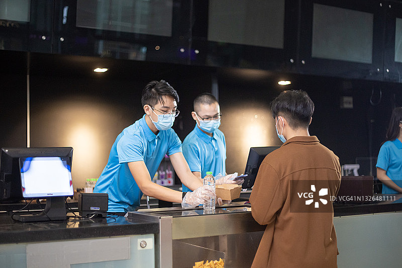 在电影院小卖部工作的亚洲电影院员工，顾客使用手机App非接触式支付图片素材