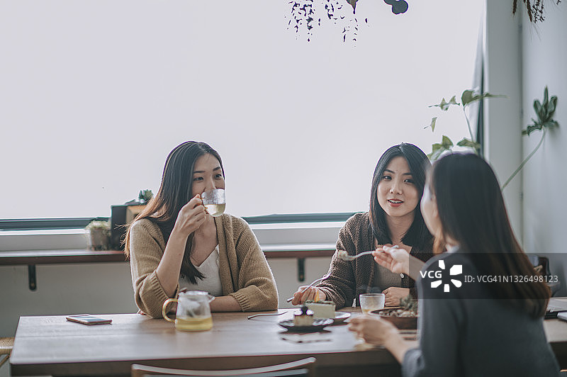 三个中国女性朋友在咖啡馆享受下午茶，分享甜点图片素材