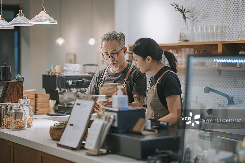 亚洲老年咖啡馆男店主在咖啡店吧台向女儿展示菜单图片素材