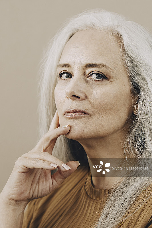 自信的中年妇女手扶椅子靠在米色背景前的肖像图片素材