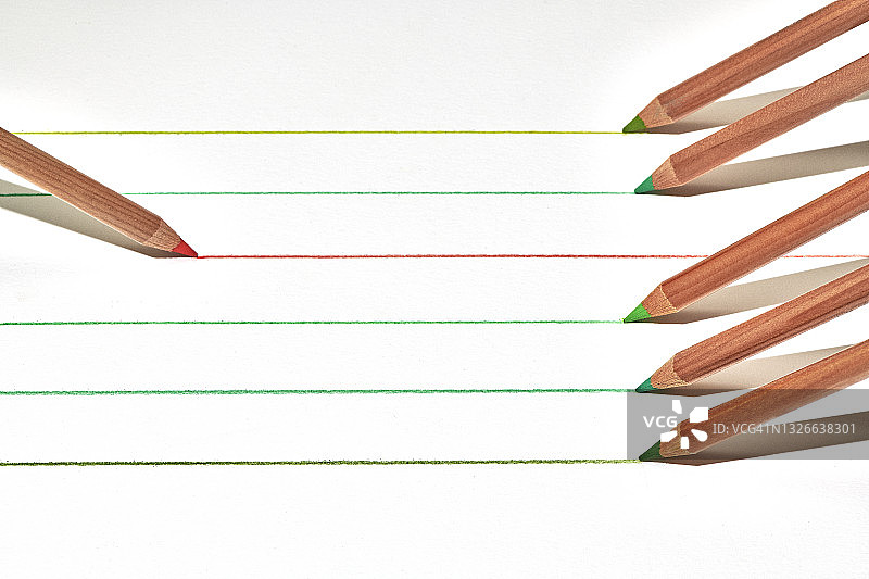 一排不同颜色的铅笔在白色纸上从左到右绘制平行线，红色铅笔从右到左绘制图片素材