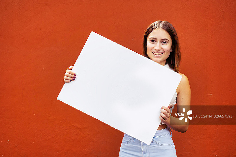 年轻的拉丁裔女人微笑着，举着空白标牌图片素材