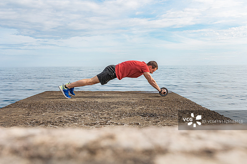 在海边用健腹轮训练的年轻运动型男士图片素材