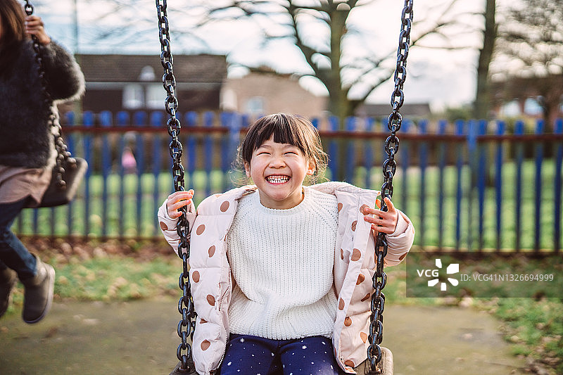 可爱的小女孩在操场上快乐地荡秋千图片素材