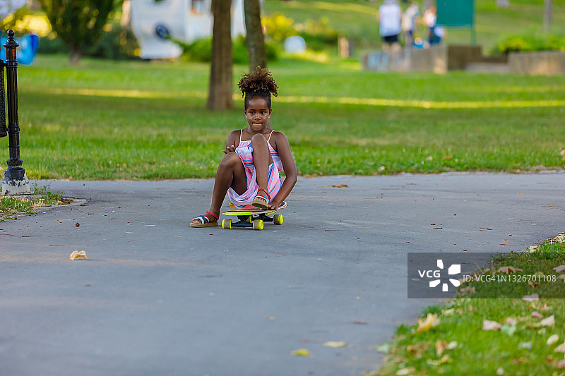坐在滑板上在公园里滑行的年轻非洲女孩图片素材