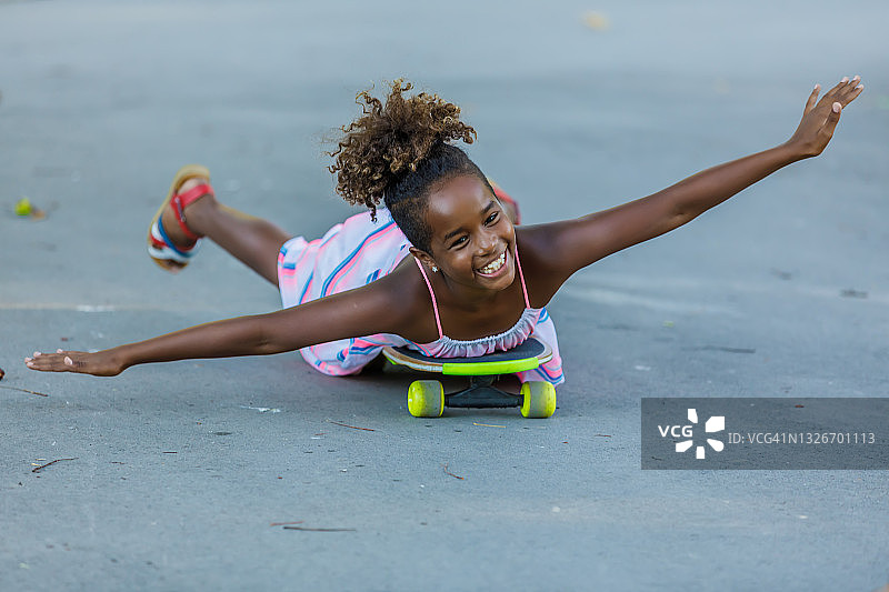 穿着连衣裙的快乐小女孩躺在长板上在公园里玩耍图片素材