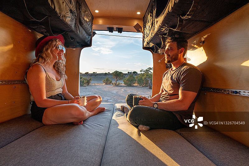年轻夫妇坐在改装面包车里，在夕阳下聊天喝咖啡图片素材
