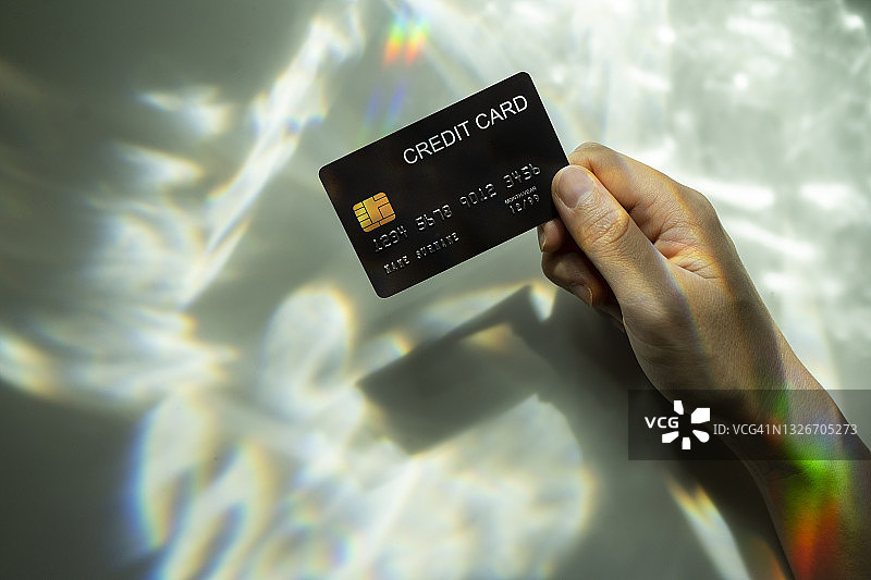 俯视视角：手持空白信用卡，另一只手用手机扫描背景光谱光影图片素材