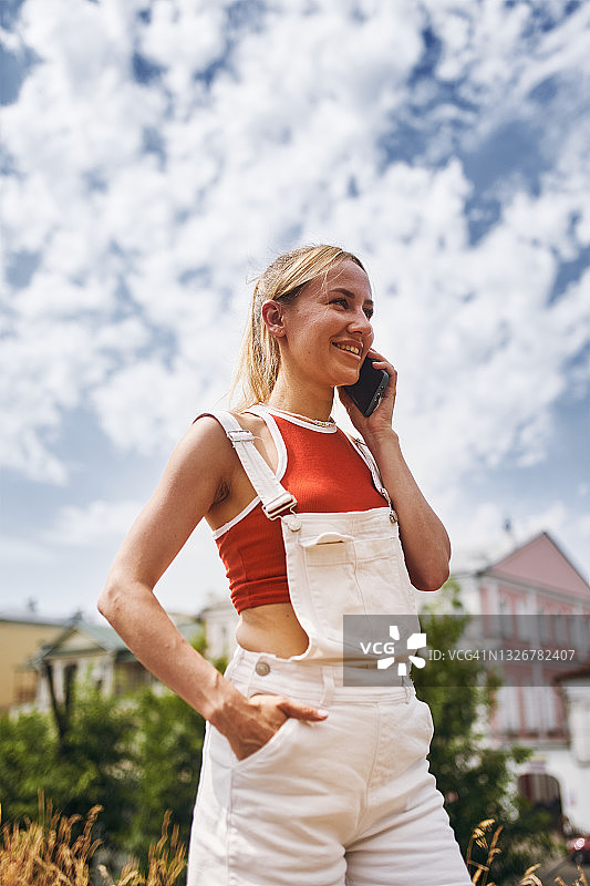 身穿红色T恤和白色工装裤的金发年轻女人在街上打电话图片素材