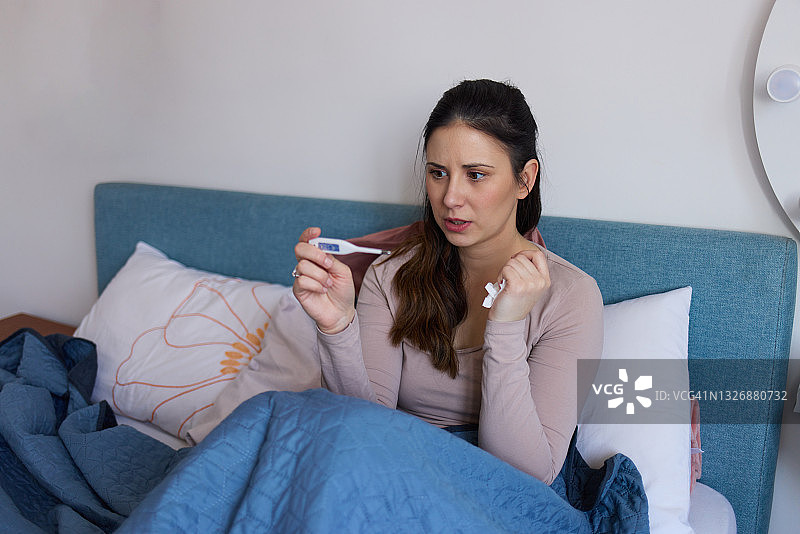 生病的女人在床上用电子体温计测量体温图片素材