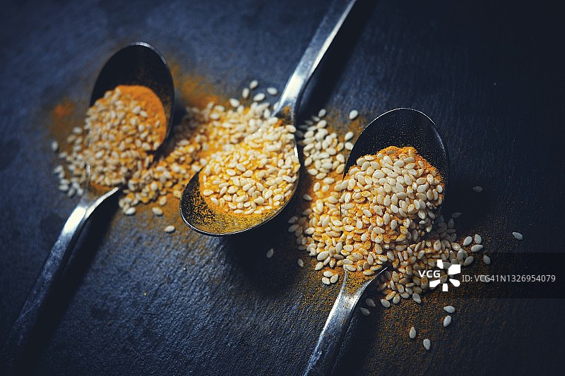 黑色背景上的姜黄香料和芝麻茶匙图片素材