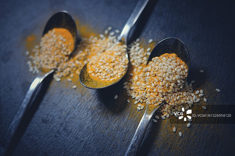 装有香料粉的勺子，黑色石板背景图片素材
